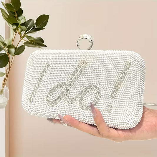 White beaded clutch with 'I Do' embellishment held by a hand against a neutral background