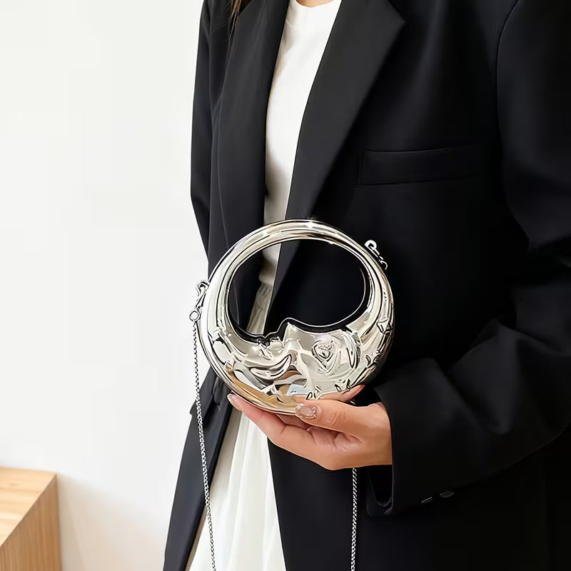 Person holding a silver clutch bag with a moon design against a plain background
