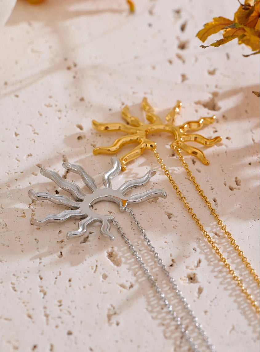 Two necklaces with sunflower pendants on a textured beige surface.