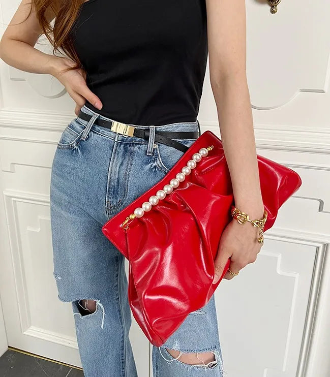 Person holding a red clutch with pearl embellishments against a white background