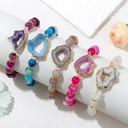 Colourful geode and bead bracelets on a white surface with a light background