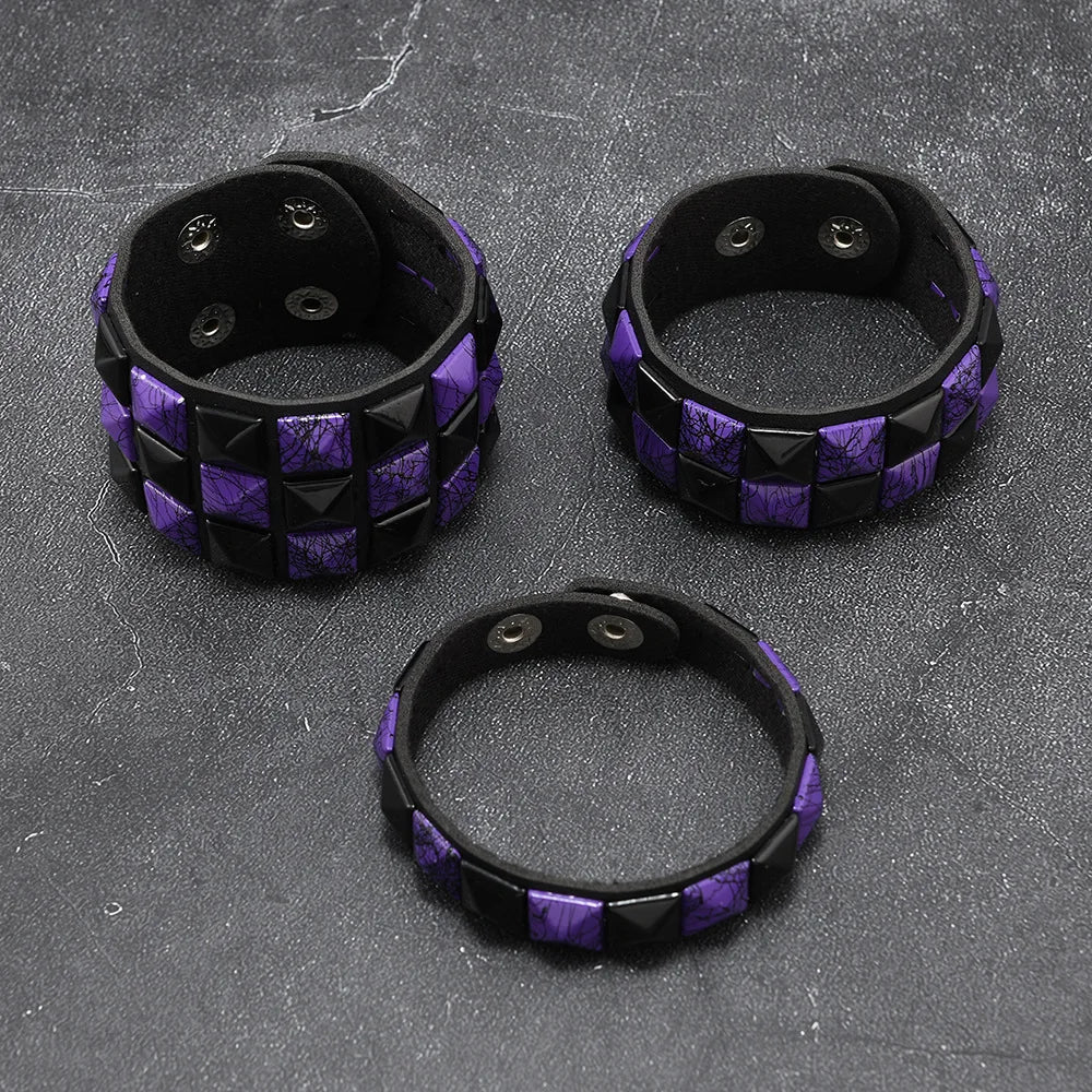 Three black and purple studded bracelets on a textured grey surface
