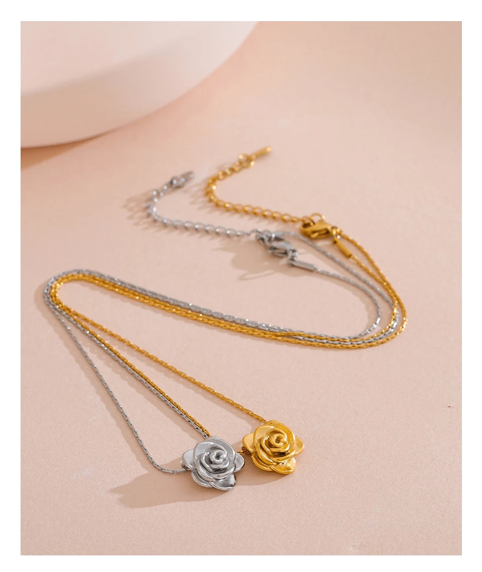 Two rose-shaped pendants on gold and silver chains against a beige background.