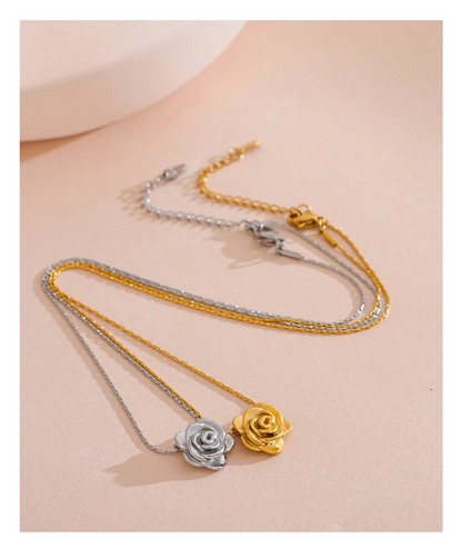 Two rose-shaped pendants on gold and silver chains against a beige background.