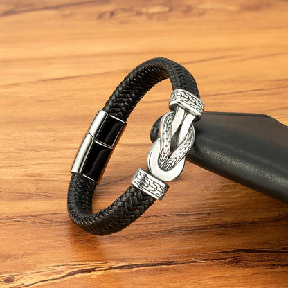Black braided leather bracelet with silver clasp on a wooden surface
