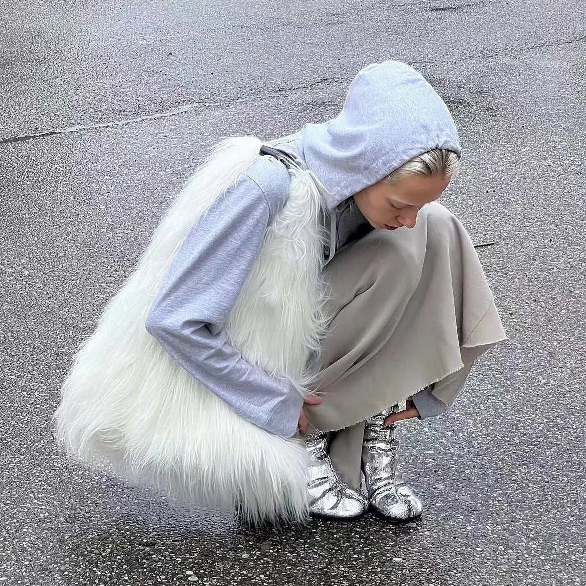 Person wearing a light blue hoodie, beige coat, and silver boots on a street.