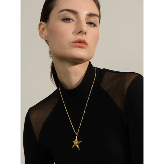 Woman wearing a black sheer top with a gold star necklace against a neutral background