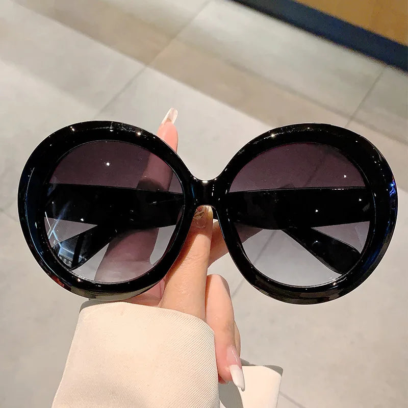 Black sunglasses held by a hand with a neutral background