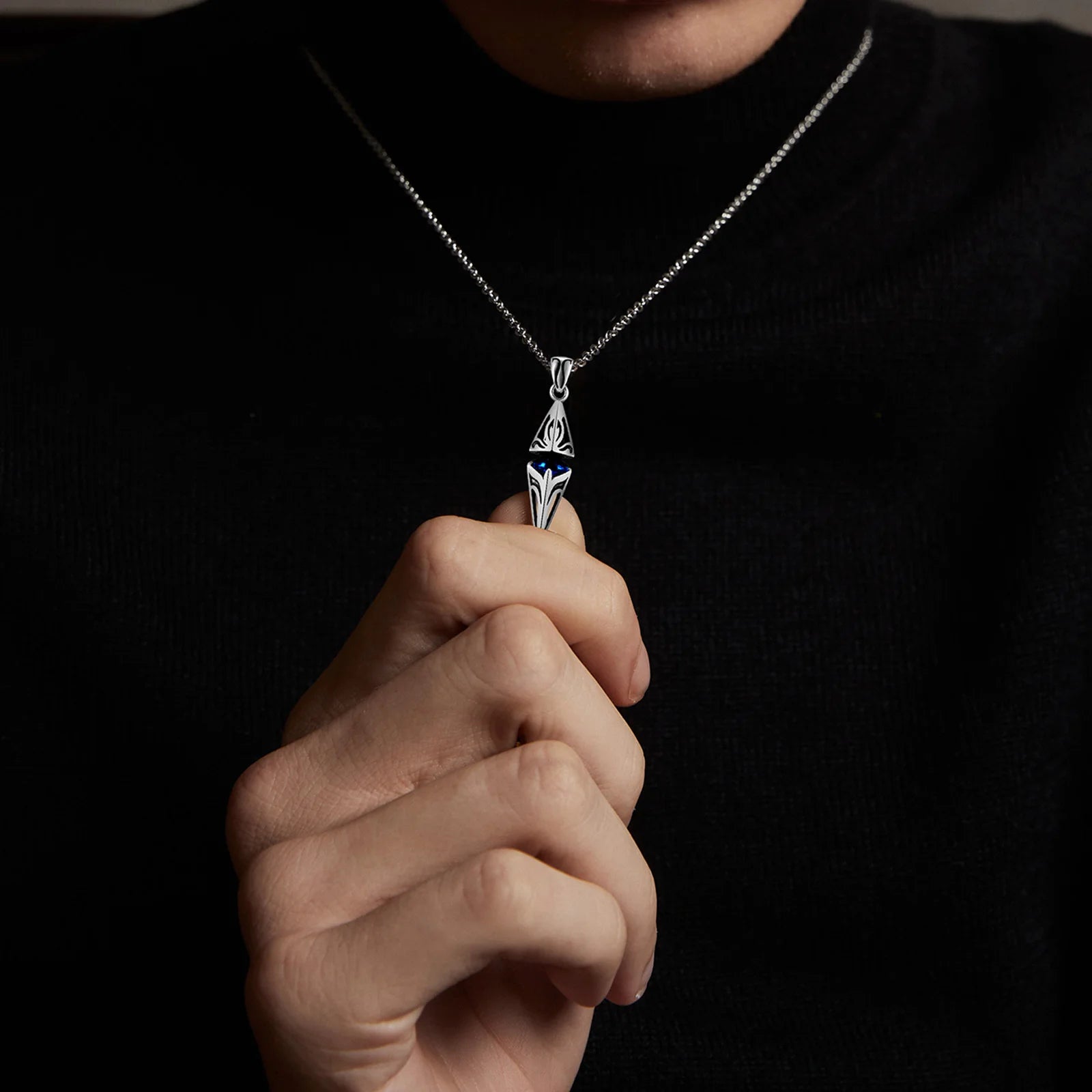Person holding a silver necklace with a pendant against a dark background