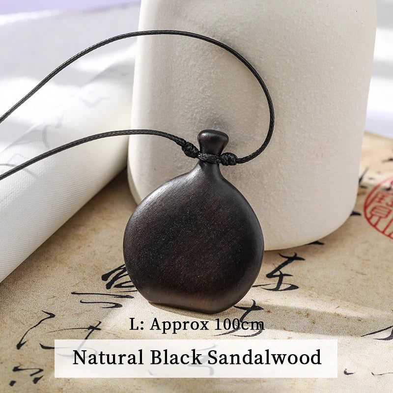 Black sandalwood pendant on a string with text indicating length and material, placed on textured surface.