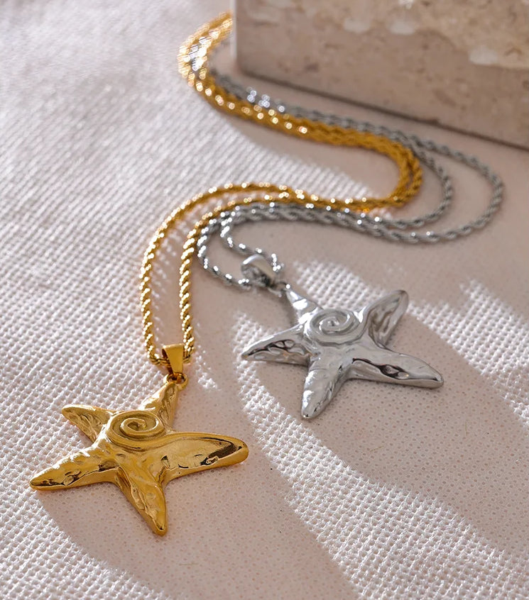Two star-shaped pendants on gold and silver chains against a textured surface.