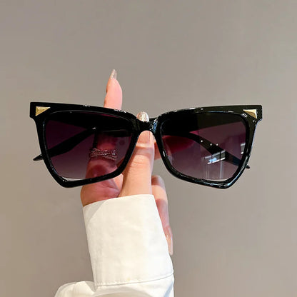 Black cat-eye sunglasses held by a hand against a neutral background
