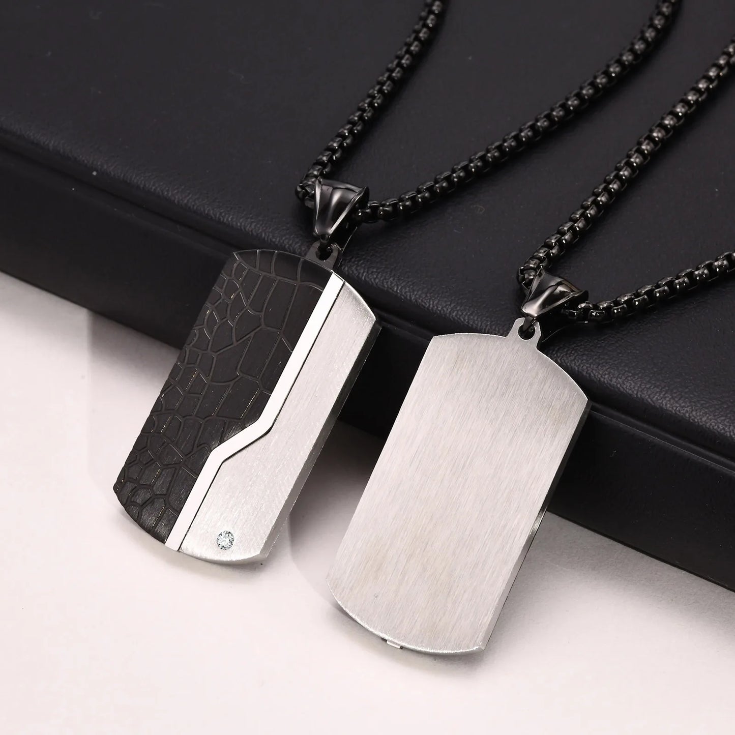 Two metallic dog tag pendants on black chains against a black background.