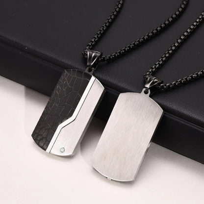 Two metallic dog tag pendants on black chains against a black background.