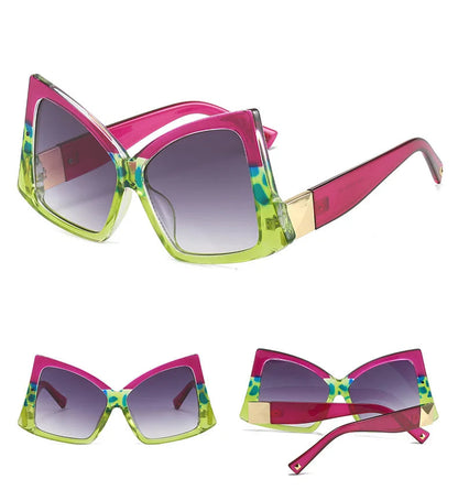 Three views of a pair of oversized cat-eye sunglasses with a bright pink and lime green frame, patterned green and blue detailing, and gold metal accents on the temples.