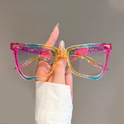 Multicoloured cat-eye glasses held by a hand against a neutral background