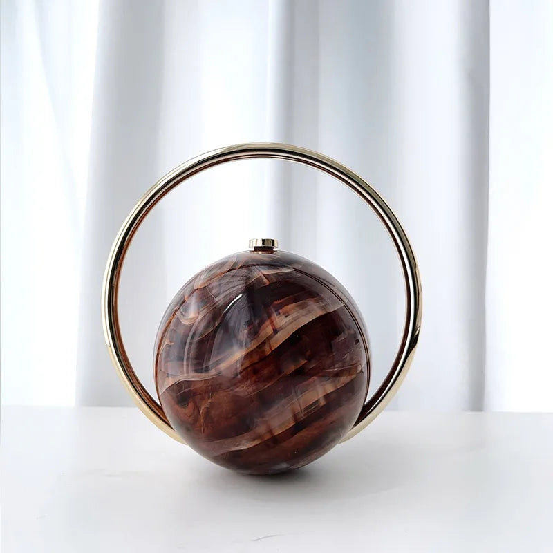 Clutch bag with a brown marbled sphere and gold circular frame on a white background