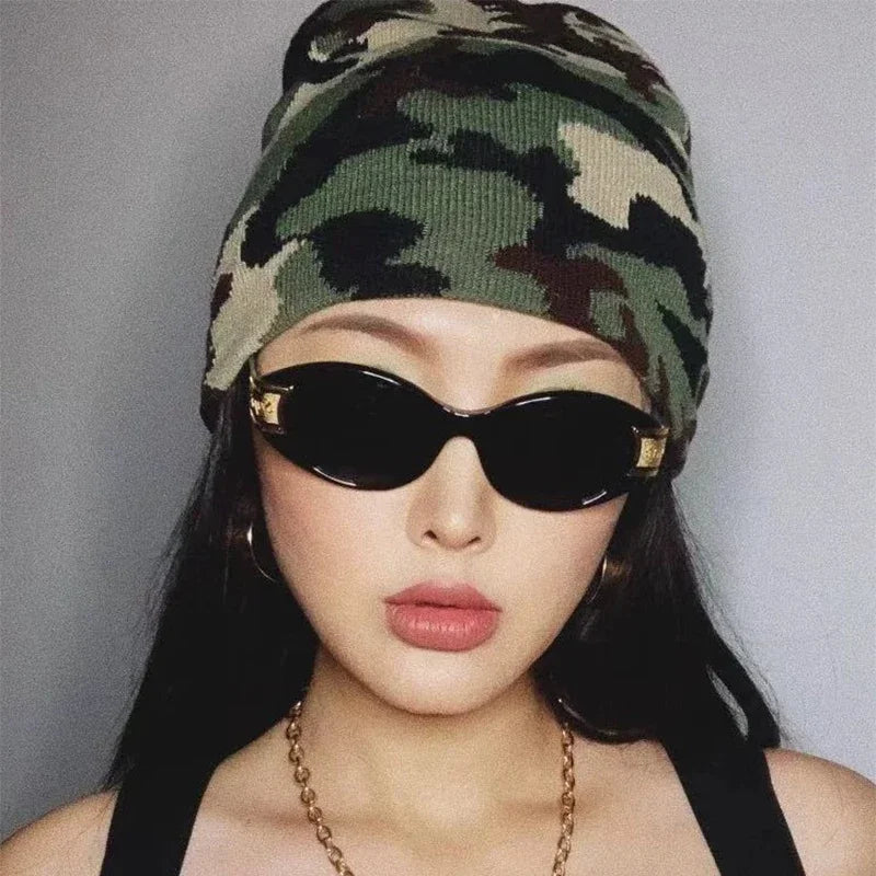 Person wearing a camouflage beanie and black sunglasses with a grey background