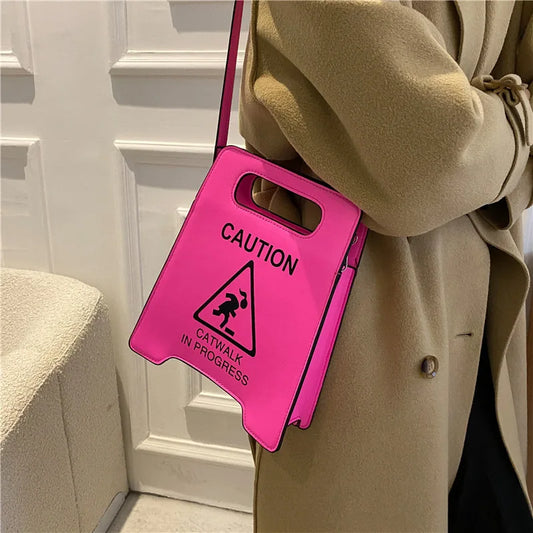 Person wearing a bright pink bag with a 'Caution: Catwalk in Progress' sign, standing against a white wall.
