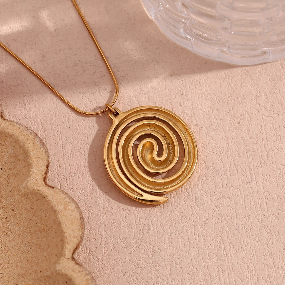 Gold spiral pendant necklace on a textured beige surface