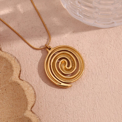 Gold spiral pendant necklace on a textured beige surface