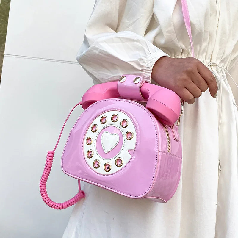 Pink phone-shaped handbag held by a person wearing a white outfit.