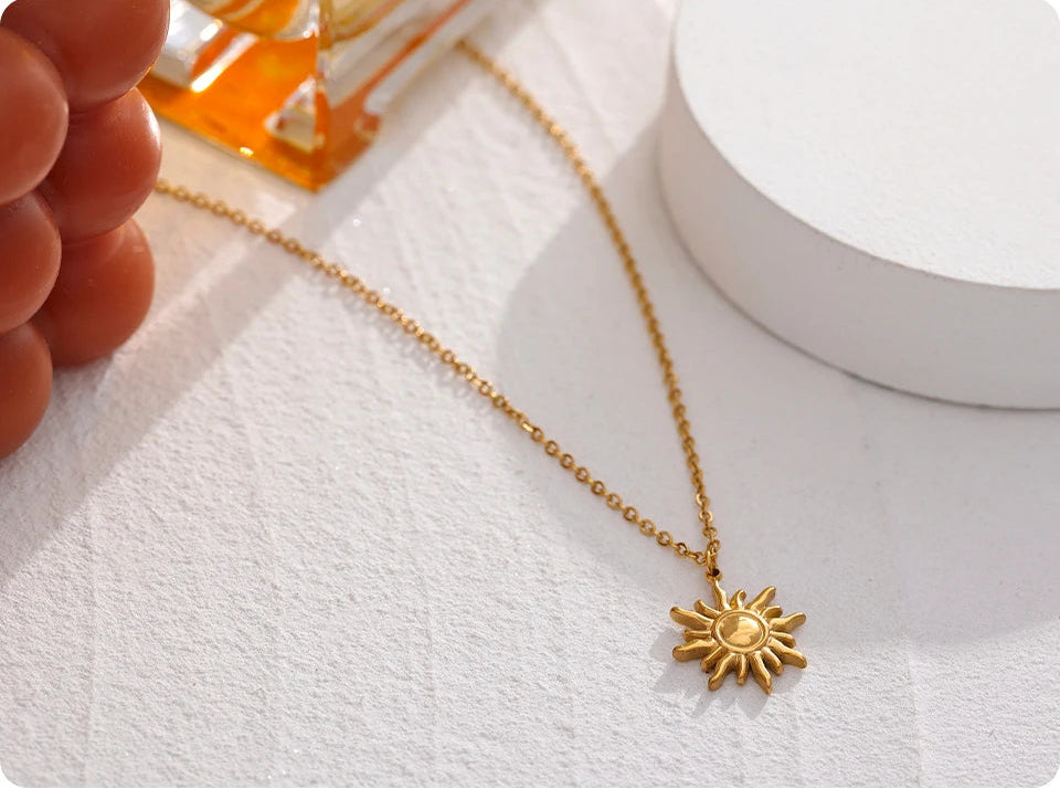 Gold necklace with a sun pendant on a white surface