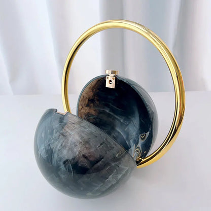 Black spherical handbag with a gold handle on a white background