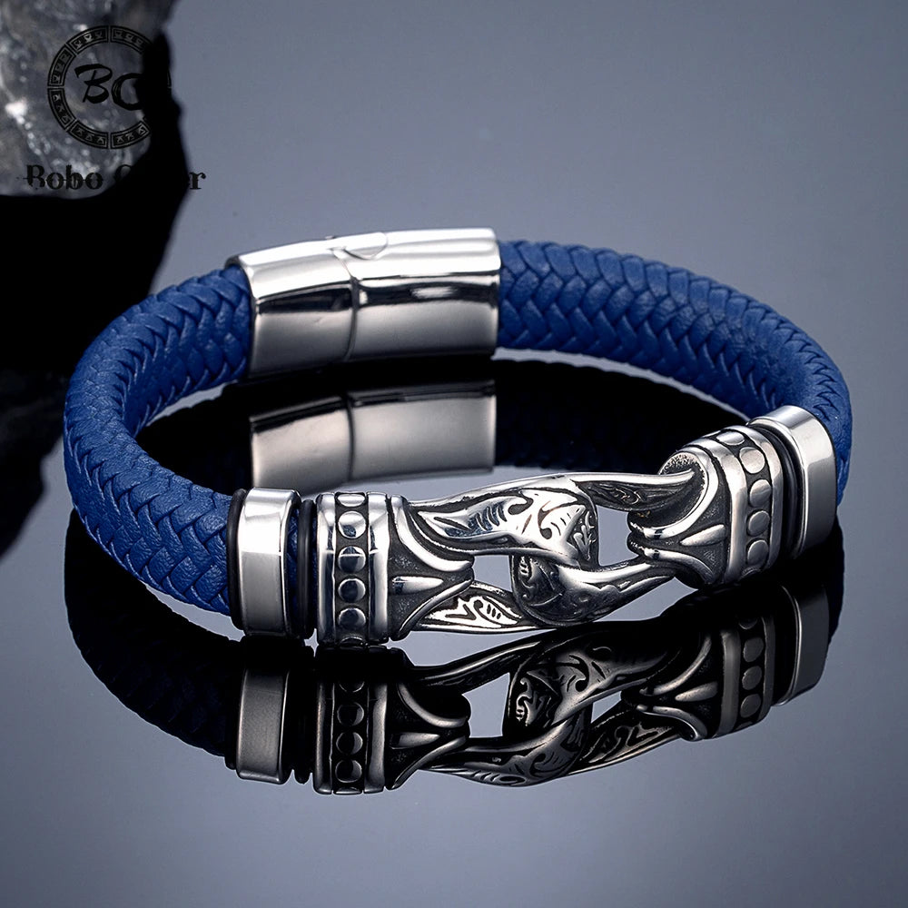 A blue braided cord bracelet with a polished silver-toned metal clasp featuring a stylized fish design, displayed on a reflective dark surface.