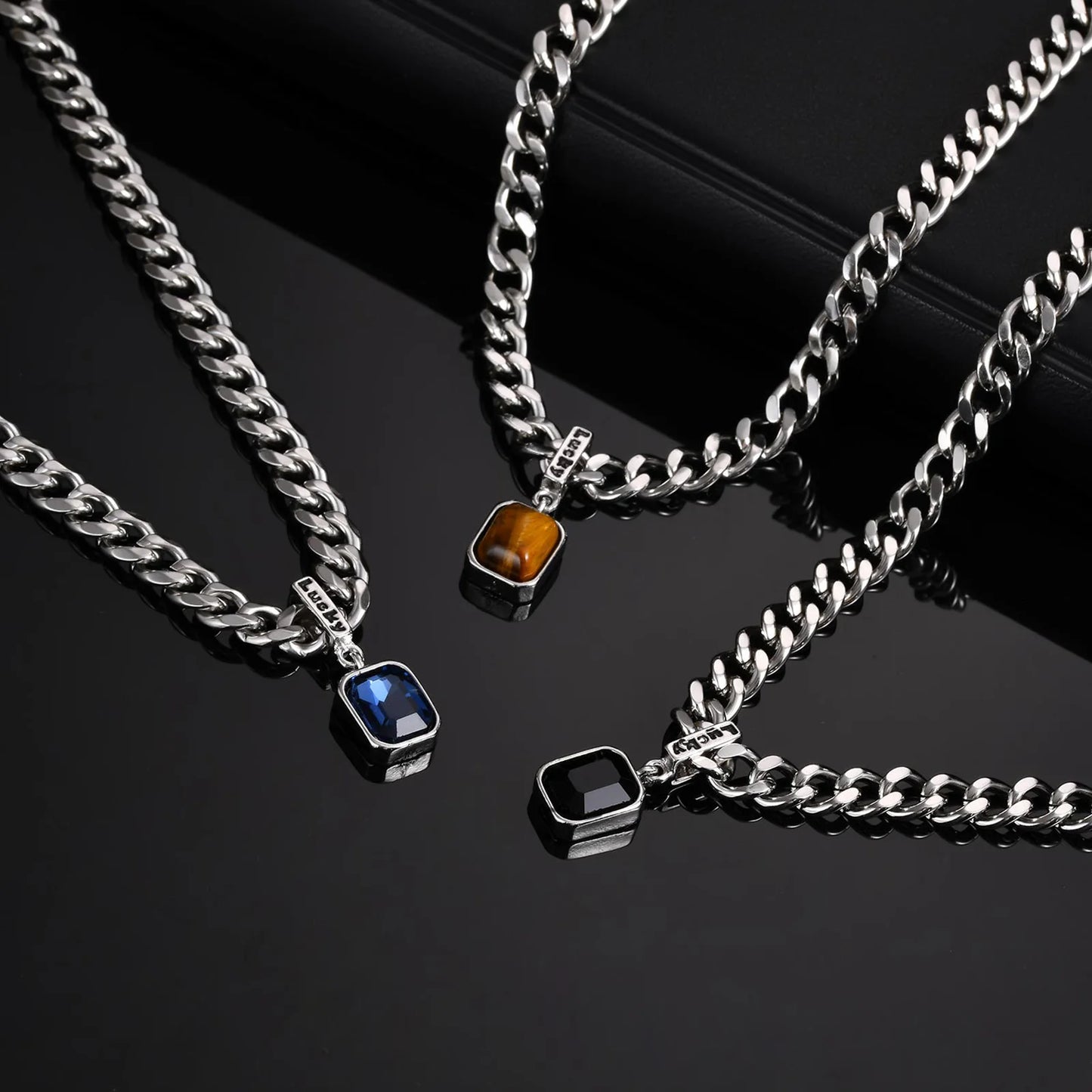 Three silver chain necklaces with gemstone pendants on a black background