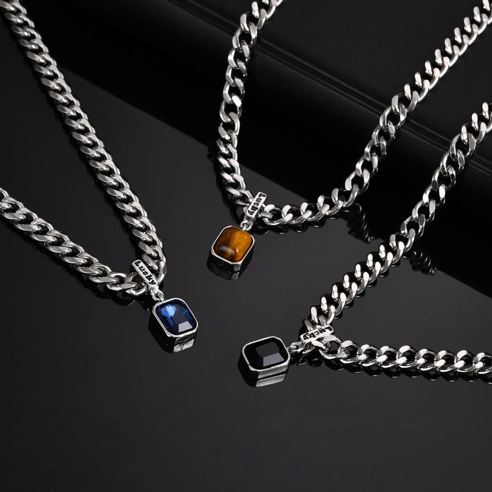 Three silver chain necklaces with gemstone pendants on a black background