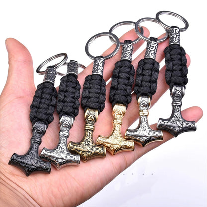 Set of Thor's hammer keychains with black braided handles held in a hand.