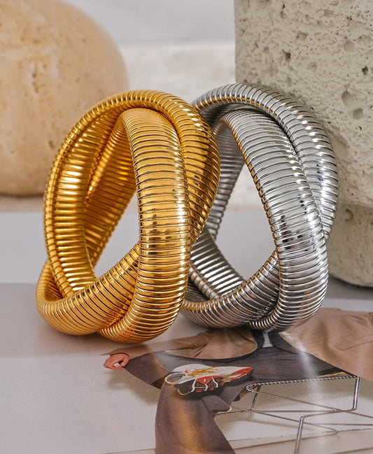Gold and silver spiral bracelets on a surface with a magazine underneath.