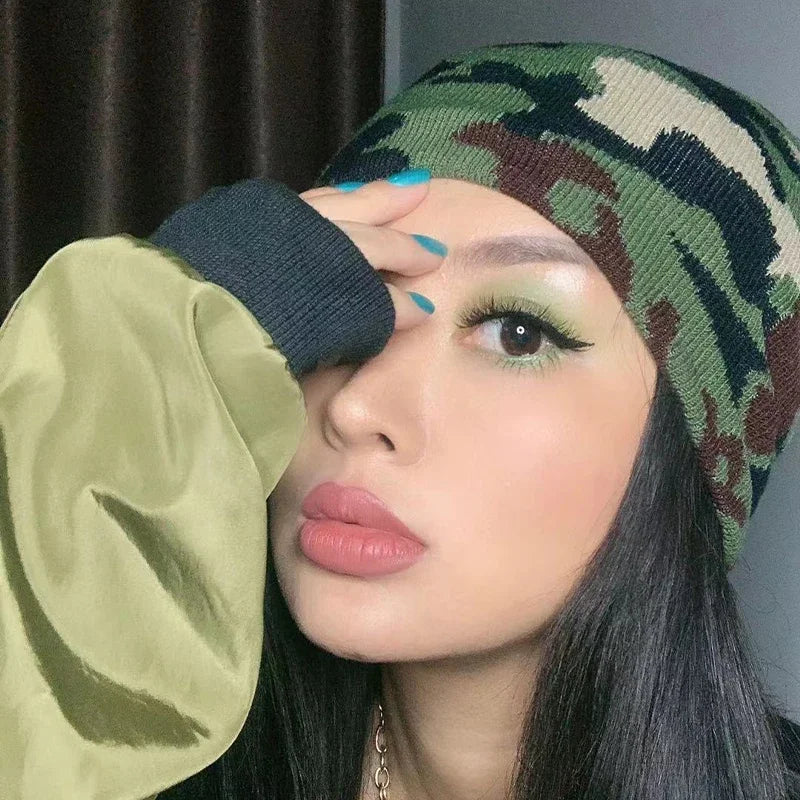 Person wearing a green camouflage beanie and green jacket with one hand on their face.