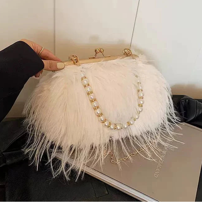 White feathered handbag with pearl detailing held by a hand against a neutral background