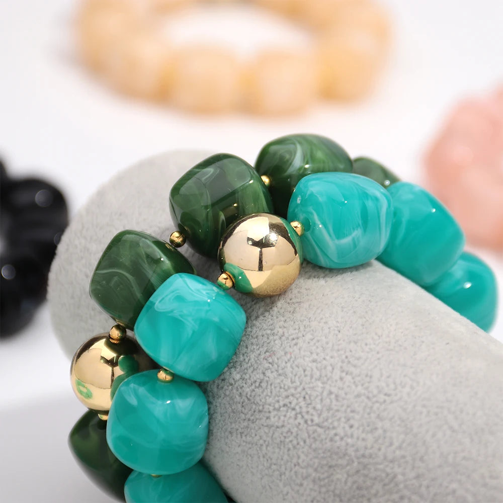 Bracelet with green and turquoise beads and gold accents on a grey surface.