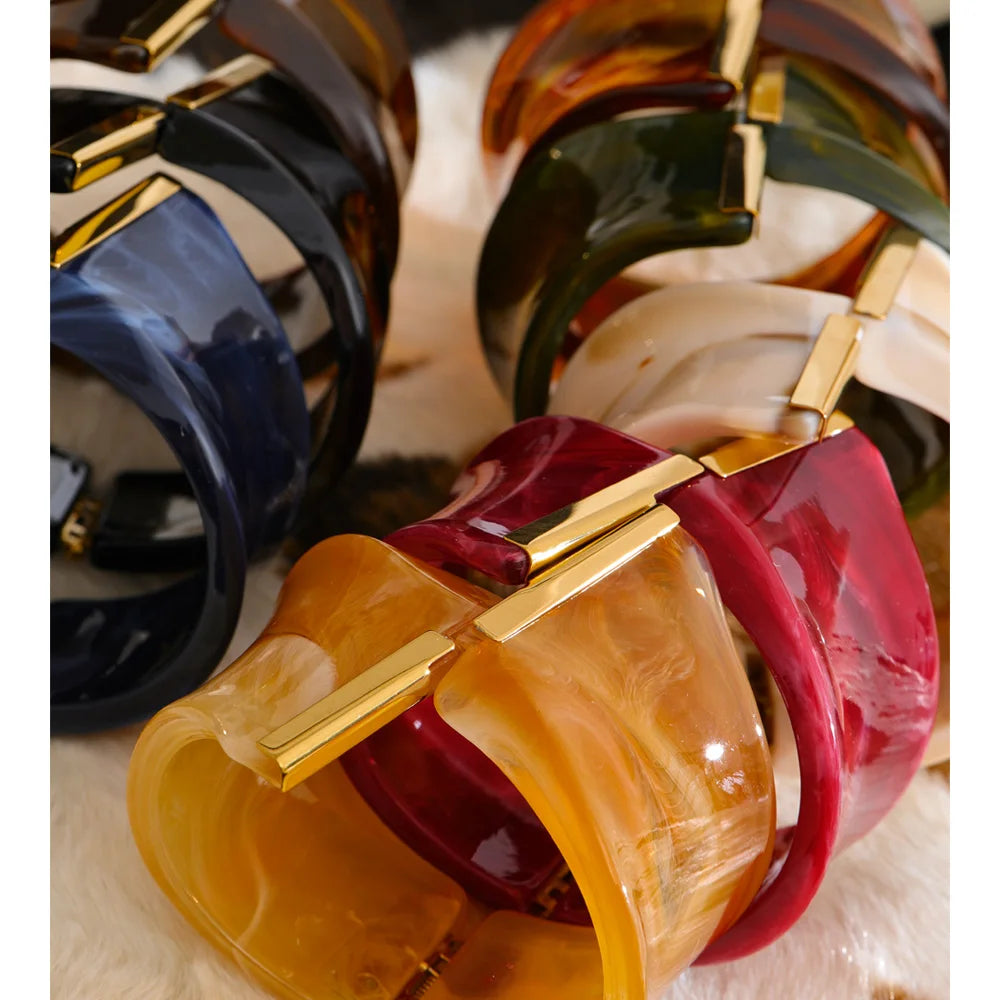 Colourful resin bracelets with gold clasps on a textured surface