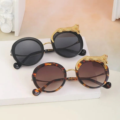 Two pairs of sunglasses with decorative leopard details on a white surface.