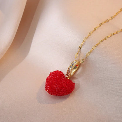 Red heart-shaped pendant on a gold chain against a soft beige background