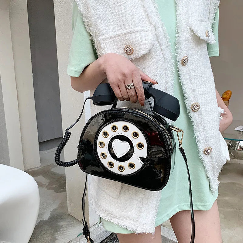 Person holding a black vintage-style phone-shaped handbag with a decorative dial.