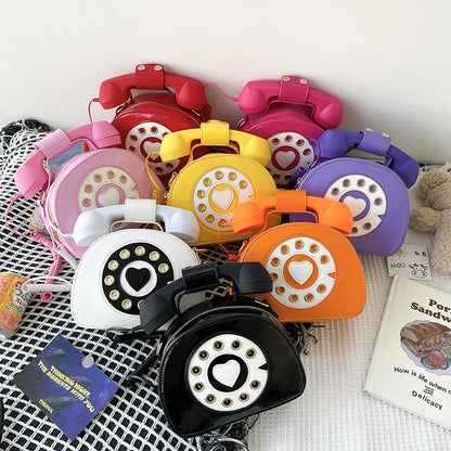 Collection of colorful rotary phone-shaped bags on a textured surface.