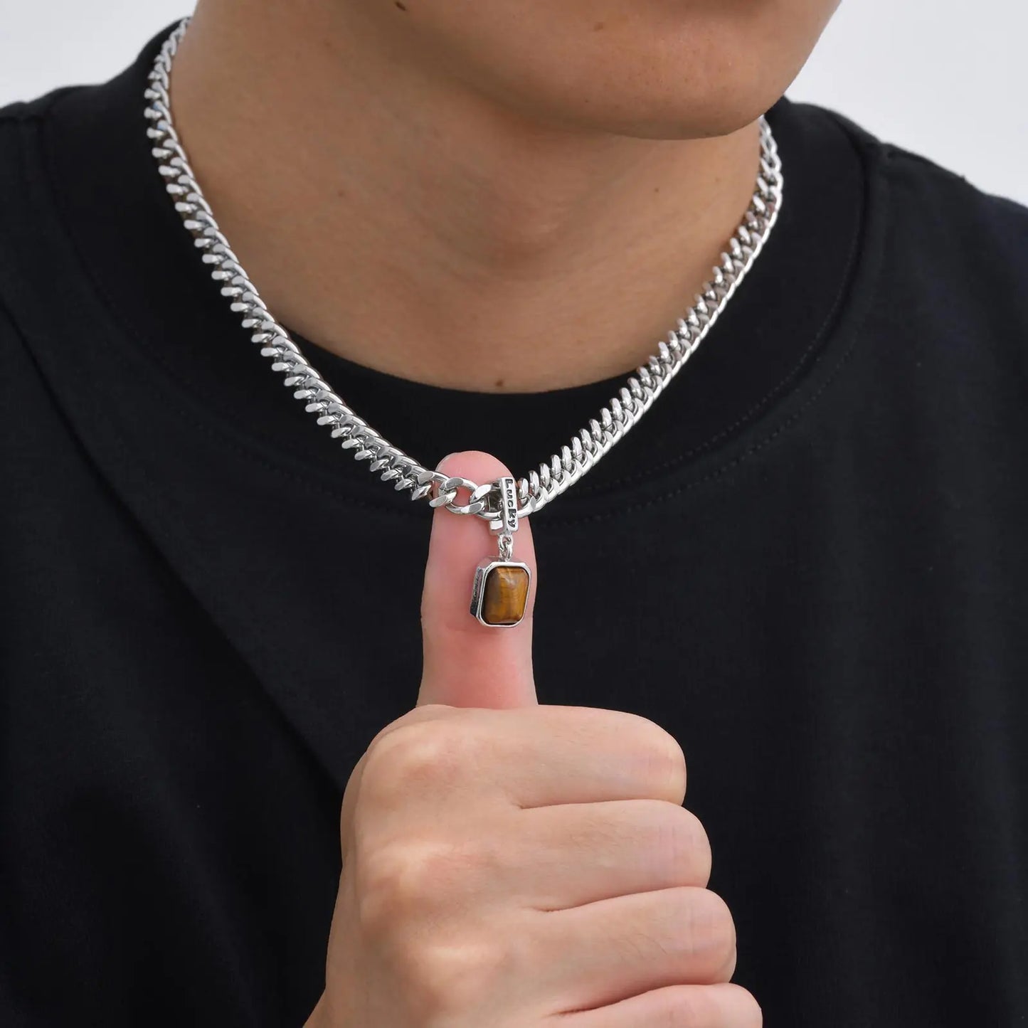 Person wearing a silver chain necklace with a tiger eye pendant, pointing to the necklace.