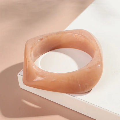 Translucent orange bracelet on a white surface with a soft pink background
