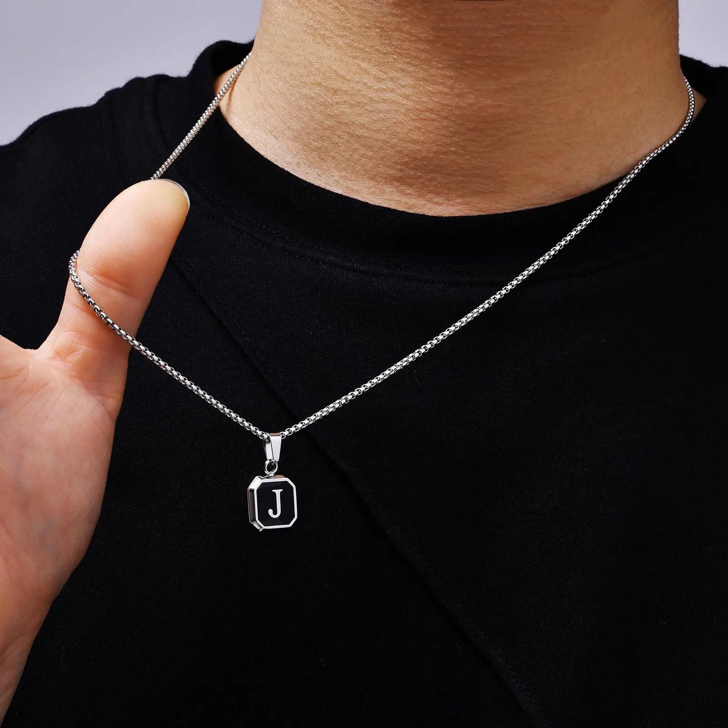 Silver necklace with a 'J' pendant worn by a person on a black shirt.