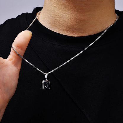 Silver necklace with a 'J' pendant worn by a person on a black shirt.