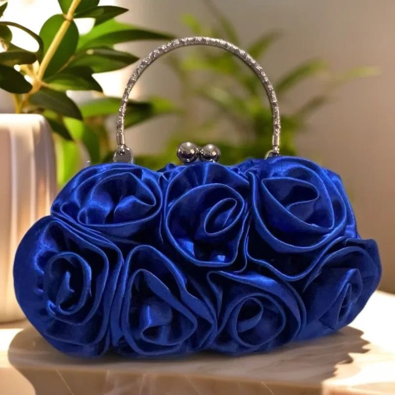 Blue rose-shaped handbag on a marble surface with a blurred green plant background