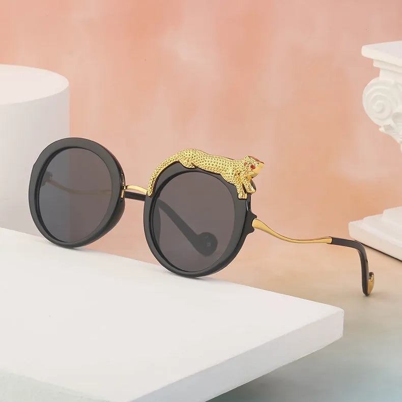 Sunglasses with a gold embellishment on a white surface with a pink background