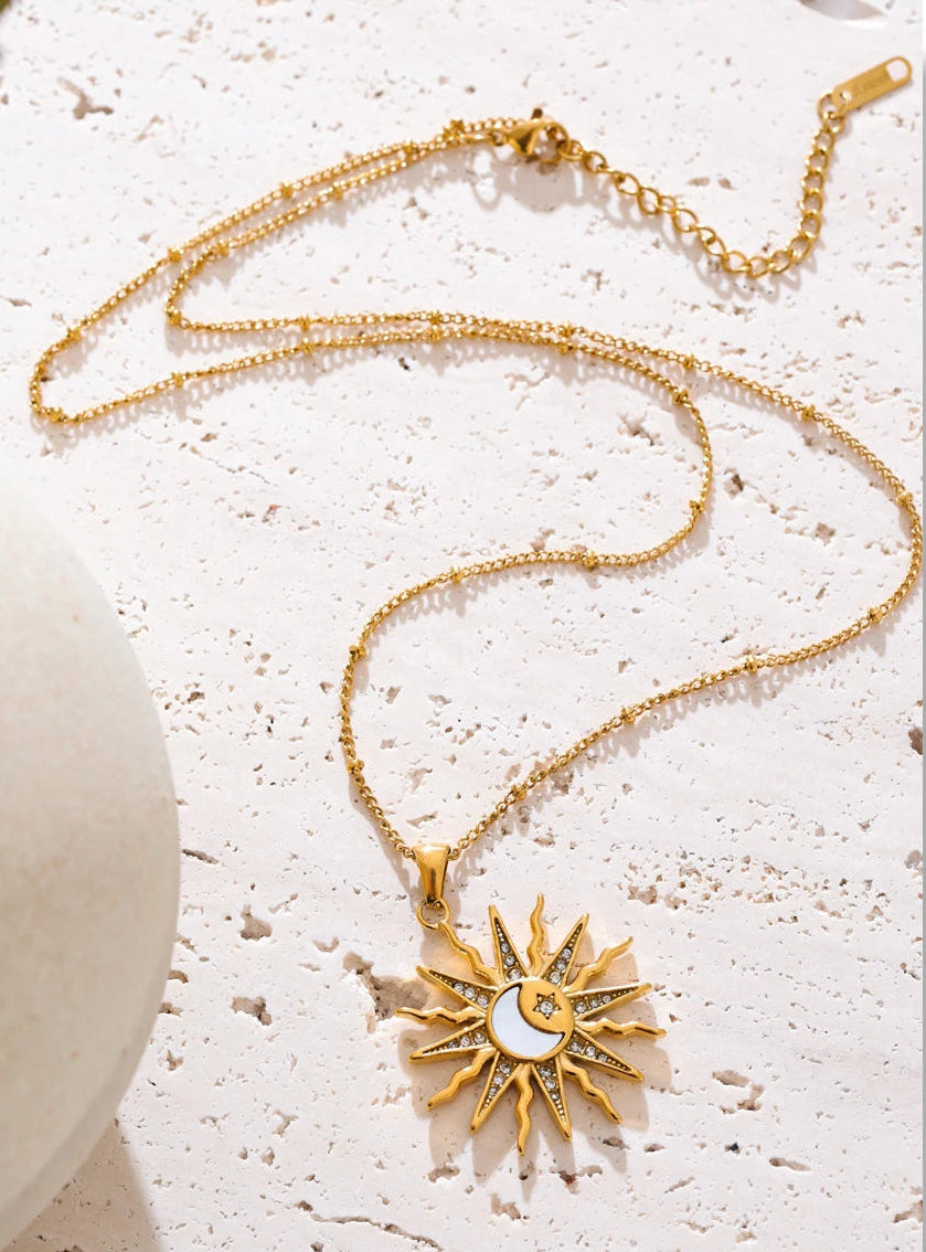 Gold necklace with a sun pendant on a textured white surface