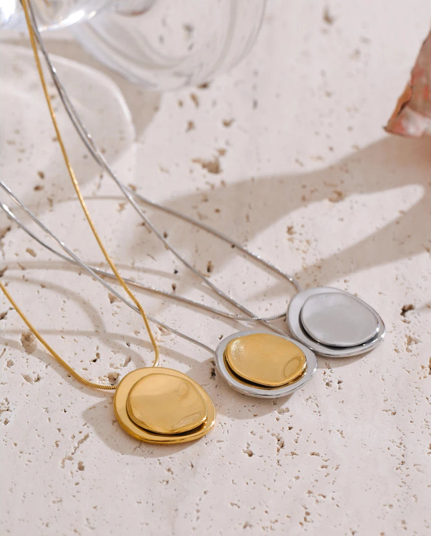 Three round pendants on a necklace against a textured beige background