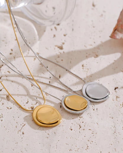 Three round pendants on a necklace against a textured beige background
